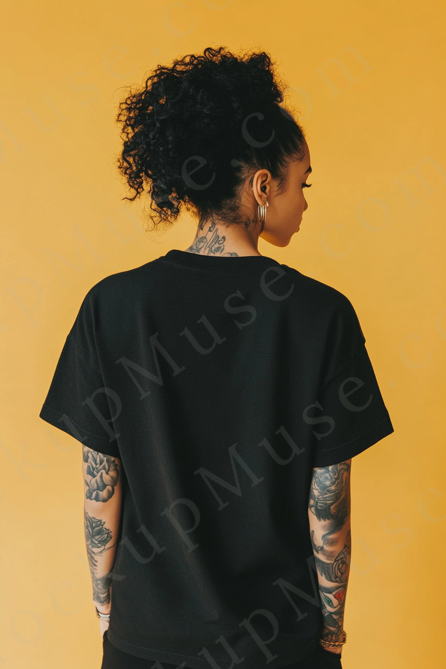 Vertical 2:3 women’s black onyx Gildan 5000 t‑shirt mockup, back view on golden‑tan studio with tattooed arms visible; clean apparel template for online stores.